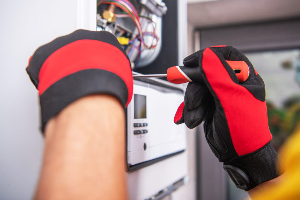 Technician's hands in red and black work gloves, repairing a broken gas heater.