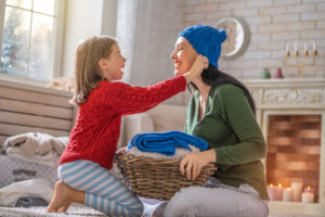 Winter portrait of happy loving family wearing knitted sweaters. Mother and child girl having fun, playing and laughing at home. Fashion concept.